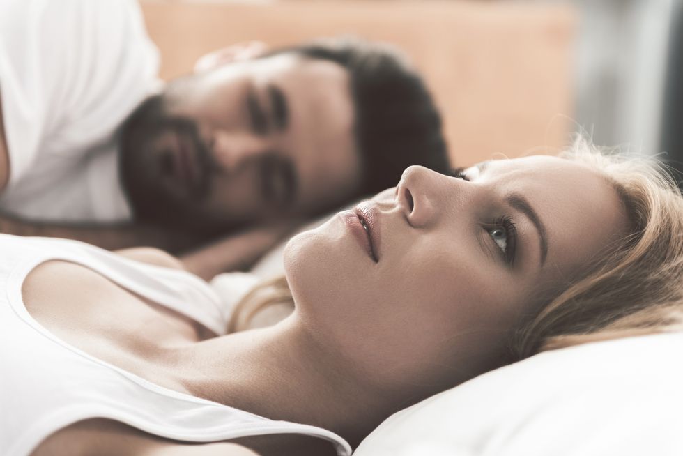 woman is lying on bed and worried about Bleeding After Sex, Her husband is sleeping on background